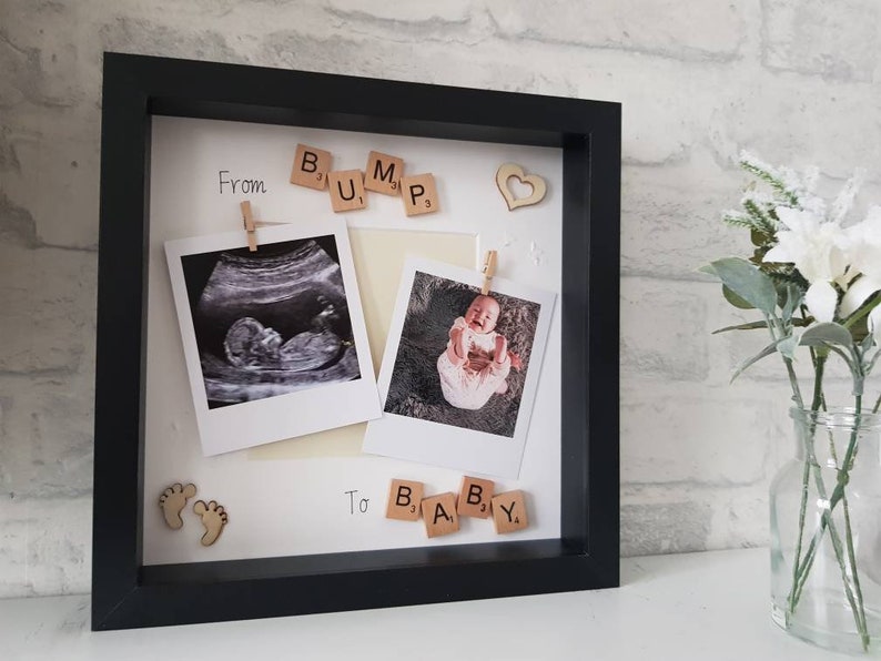 Pu&ograve; includere: Una cornice nera con due foto, un'ecografia e una foto di un bambino. Le lettere di legno compongono le parole "BUMP" e "BABY". Sono inclusi anche un cuore e delle impronte di legno decorativi.