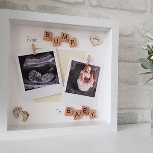 May include: A white picture frame with a white mat. The frame has two photos inside, one of an ultrasound image and one of a baby. The photos are held in place with small wooden pegs. The frame also has a wooden heart, wooden baby feet, and wooden letter tiles that spell out 'From Bump to Baby'.