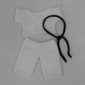 May include: White knitted doll clothes set with a black belt. The set includes a short-sleeved top with a wrap-around closure and a pair of shorts.