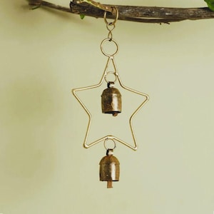 Peut inclure: Un carillon éolien en forme d'étoile en métal doré avec deux petites cloches. L'étoile a un design simple et ouvert. Les cloches sont d'une couleur or antique plus foncée et pendent des pointes de l'étoile. Le carillon est suspendu à une branche d'arbre.