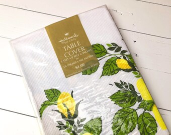 May include: A white Hallmark table cover with a floral design featuring large yellow roses and green leaves. The cover is 5 feet by 8 feet 6 inches (60 inches x 102 inches). The packaging includes the text "TABLE COVER".