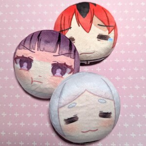Peut inclure: Trois jouets en peluche ronds avec des visages de dessins animés. Le premier jouet a les cheveux roux et une expression triste. Le deuxième jouet a les cheveux violets et une expression en colère. Le troisième jouet a les cheveux blancs et une expression neutre.