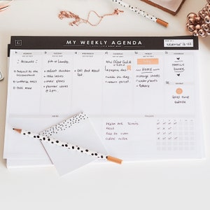 Op de afbeelding: Een zwart-witte weekplanner met een zwart-witte notitieblok met stippen en een potlood erop. De planner heeft een sectie voor elke dag van de week en bevat een tracker voor gewoontes. De tekst op de planner luidt "My Weekly Agenda" en "November 16-22".