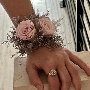 May include: A wrist corsage with two blush pink roses and dried brown foliage.