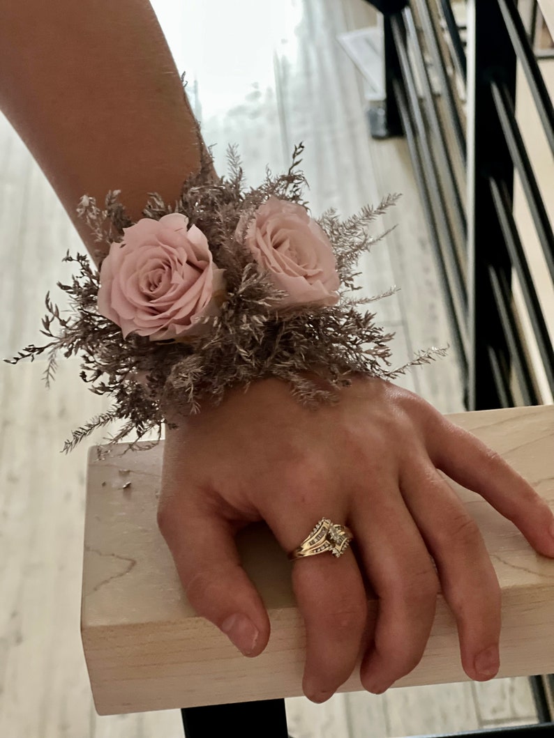 May include: A wrist corsage with two blush pink roses and dried brown foliage.
