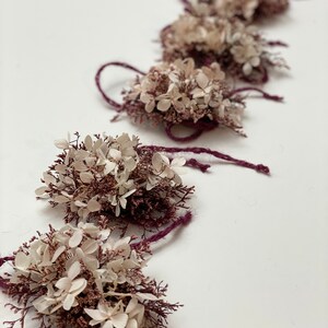 May include: A string of dried flower arrangements with white and pink flowers tied with burgundy twine.