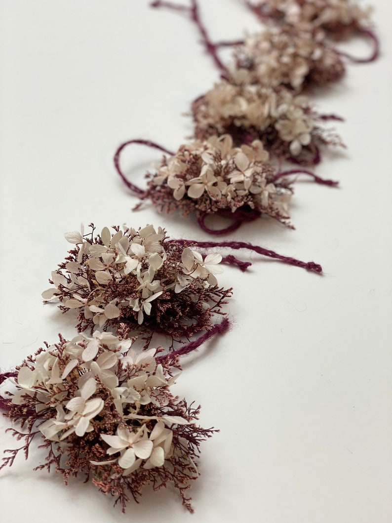 May include: A string of dried flower arrangements with white and pink flowers tied with burgundy twine.