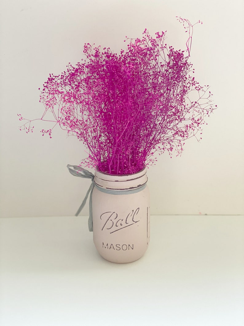 May include: A pink mason jar with the text "Ball Mason" on the front, filled with a bouquet of pink dried flowers.