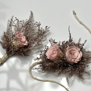 May include: Two small bouquets of dried flowers with pink roses and brown dried grasses. The bouquets are tied with twine and are connected by a long piece of twine.