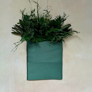 May include: A green fabric pouch with a variety of dried green plants and leaves inside.