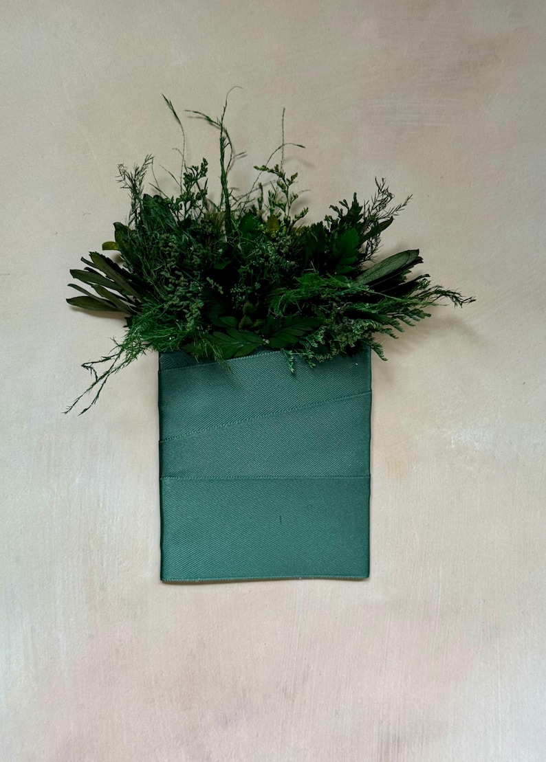 May include: A green fabric pouch with a variety of dried green plants and leaves inside.