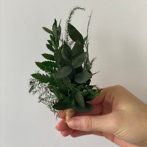 May include: A small bouquet of green foliage tied with twine. The bouquet includes ferns, eucalyptus, and other greenery.