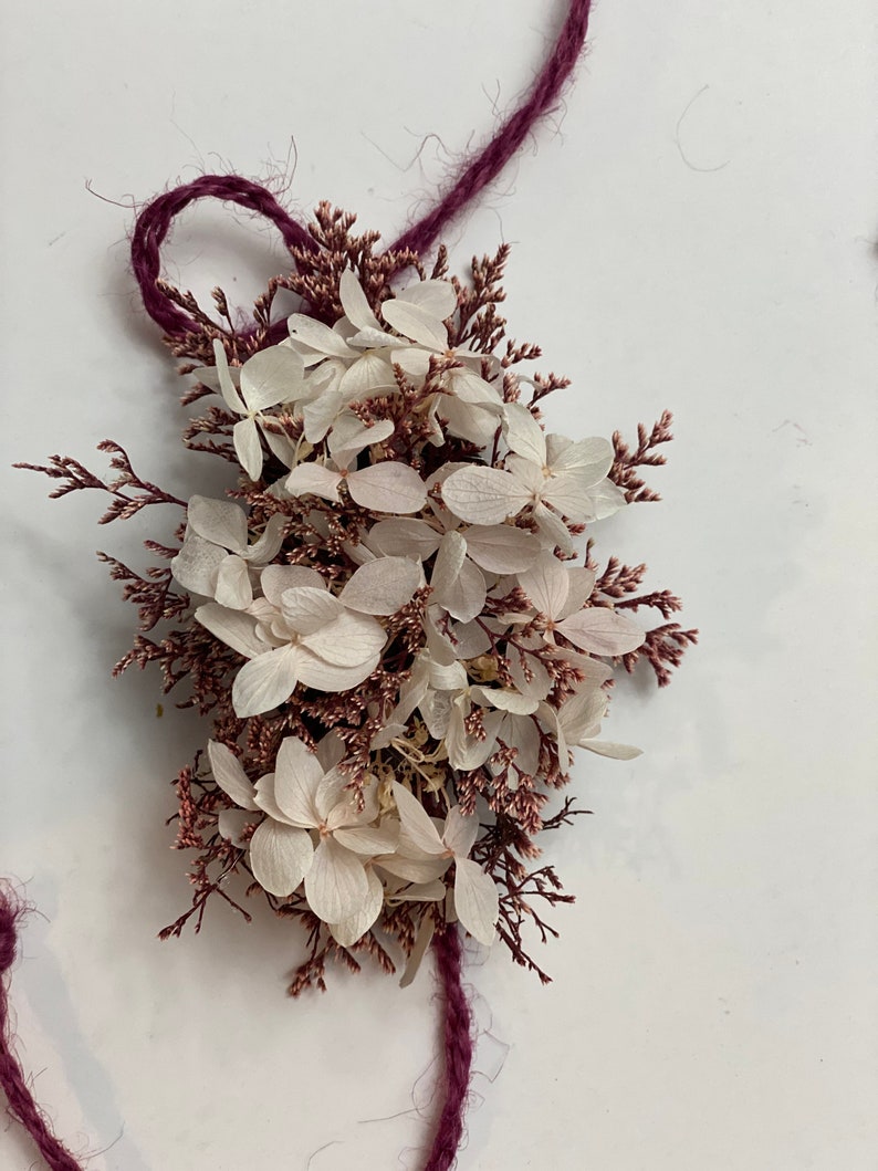 May include: A bouquet of dried white hydrangea flowers with pink stems tied together with a burgundy twine.