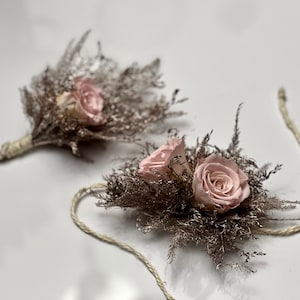 May include: Two delicate floral wrist corsages with pink roses and dried grasses, tied with twine.