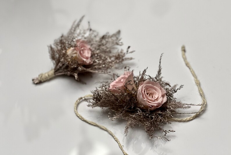 May include: Two delicate floral wrist corsages with pink roses and dried grasses, tied with twine.