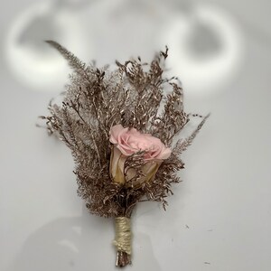 May include: A small bouquet of dried flowers with a single pink rose in the center. The bouquet is tied with twine and has a rustic, natural look.