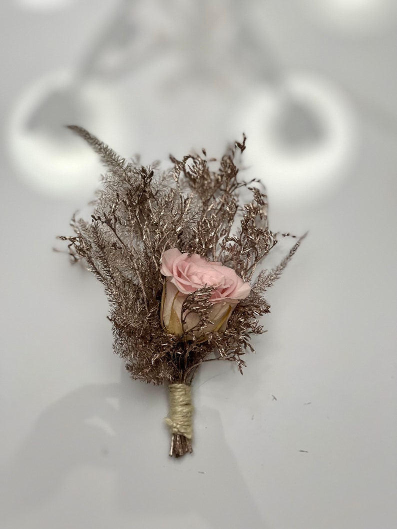 May include: A small bouquet of dried flowers with a single pink rose in the center. The bouquet is tied with twine and has a rustic, natural look.