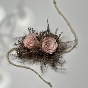 May include: Two pink roses are nestled in a bed of dried brown foliage, tied together with a natural twine string.