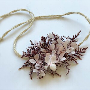May include: A delicate floral crown made of dried pink and burgundy flowers and greenery, tied with a natural twine string.