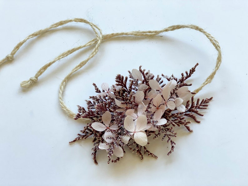 May include: A delicate floral crown made of dried pink and burgundy flowers and greenery, tied with a natural twine string.