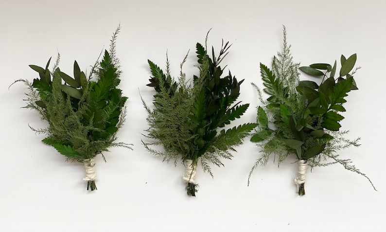 May include: Three small bouquets of greenery, each tied with twine. The bouquets are made up of ferns, eucalyptus, and other leafy sprigs.