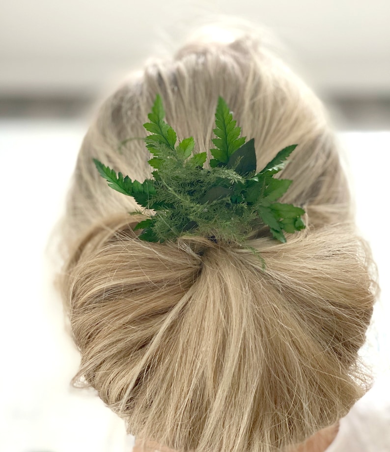 May include: A green fern hair clip with a simple design. The clip is worn in a woman's blonde hair.