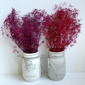 Peut inclure: Deux bocaux en verre Mason peints en blanc avec le mot "Ball" et "Mason" imprim&eacute; dessus. Les bocaux sont remplis de fleurs s&eacute;ch&eacute;es roses et rouges.