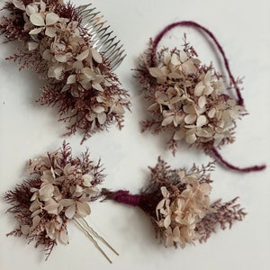 May include: Set of four hair accessories featuring dried flowers in shades of white and burgundy. The set includes a comb, a headband, and two bobby pins.
