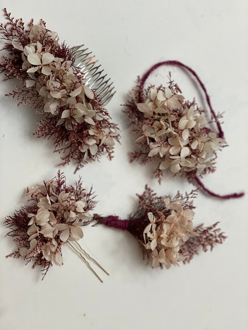 May include: Set of four hair accessories featuring dried flowers in shades of white and burgundy. The set includes a comb, a headband, and two bobby pins.