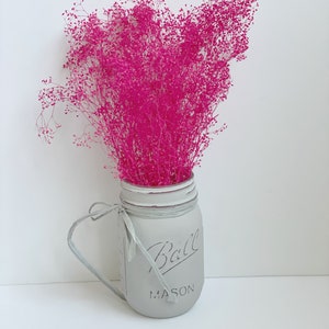 May include: A gray painted mason jar with a white ribbon and the text "Ball Mason" on the front. The jar is filled with pink dried flowers.
