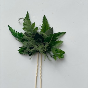 May include: A pair of gold hair pins with a cluster of green leaves and ferns attached.