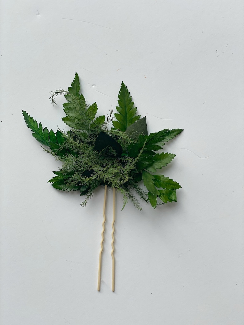 May include: A pair of gold hair pins with a cluster of green leaves and ferns attached.