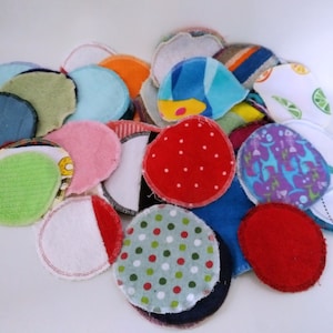 Op de afbeelding: Een verzameling kleurrijke, herbruikbare wattenschijfjes in diverse patronen en kleuren. De schijfjes bevatten effen kleuren zoals rood en blauw, en patronen met stippen, strepen en bloemmotieven. De randen zijn afgewerkt met stiksels.
