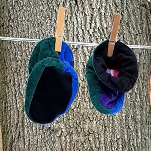 May include: Two pairs of black, blue and green corduroy baby booties hanging on a washing line with wooden clothes pegs.
