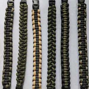 May include: Six paracord bracelets in various green, black, and tan color combinations. The bracelets are made with a woven pattern and have black plastic clasps.