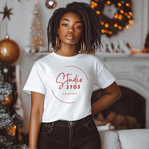 May include: A woman wearing a white t-shirt with a red circle logo that says "Studio 3703 Company".