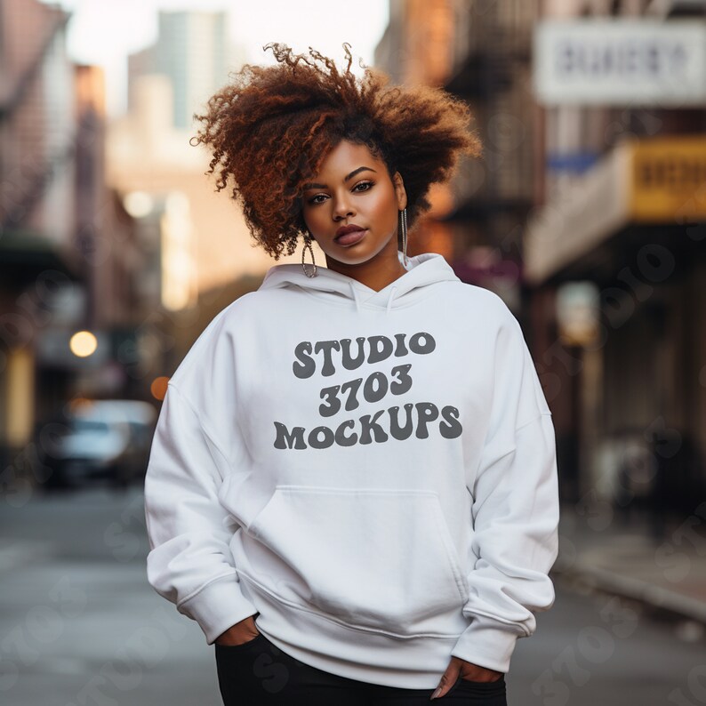 K&ouml;nnte beinhalten: Ein wei&szlig;er Hoodie mit dem Text "STUDIO 3703 MOCKUPS" in einer Retro-Schrift. Das Model tr&auml;gt den Hoodie und hat lockiges braunes Haar.