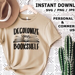 Könnte beinhalten: Ein beiges T-Shirt mit dem Text "DECOLONIZE your BOOKSHELF" in schwarzer Schrift. Das Shirt liegt auf einem weißen Hintergrund mit einem schwarz-weißen Muster.