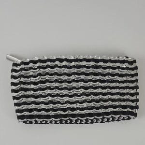 Puede incluir: Clutch rectangular hecha a mano con anillas de latas de aluminio recicladas. La cartera presenta un patrón repetitivo de anillas plateadas y tela negra, con cierre de cremallera plateada. Un accesorio único y ecológico.