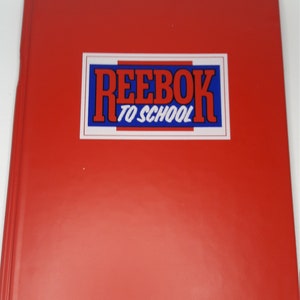 Puede incluir: Carpeta roja con una pegatina azul y blanca que dice "Reebok To School"