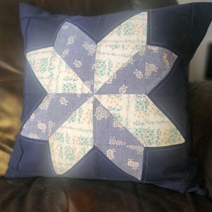 Puede incluir: Cojín cuadrado azul marino con un diseño de estrella. La estrella está hecha de tela azul claro y blanca con un estampado floral. La almohada es un artículo decorativo.