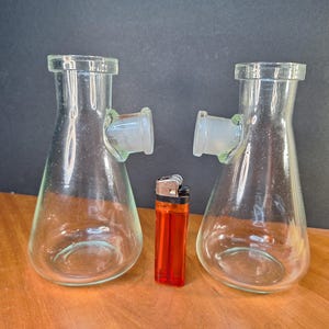 May include: Two clear glass beakers with side arms and a red lighter. The beakers are empty and have a round bottom.