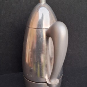 May include: A silver, stovetop espresso maker with a rounded, teardrop-shaped design and a long, curved handle.