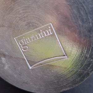 May include: A silver metal bottom of a pot with the word "giardini" embossed on it.