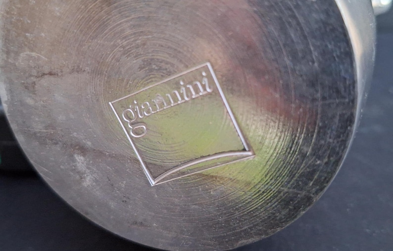 May include: A silver metal bottom of a pot with the word "giardini" embossed on it.