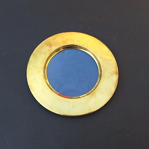 May include: A round, brass-colored picture frame with a blue interior. The frame has a wide, circular border and a smooth, polished finish. The blue interior provides a contrasting backdrop.
