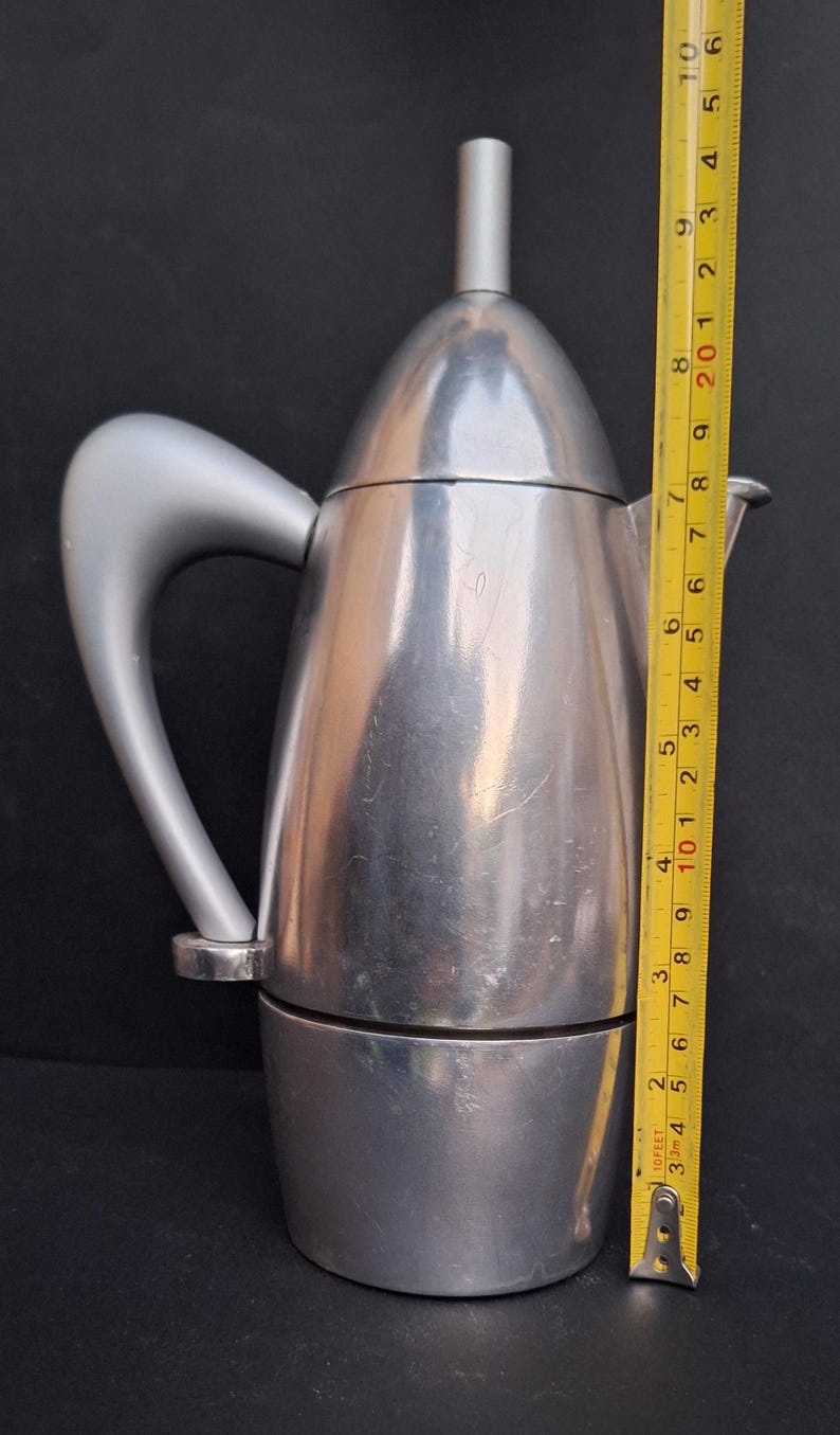 May include: A silver-colored stovetop espresso maker with a curved handle. The maker is 9 inches tall.