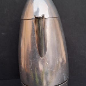 May include: A silver aluminum stovetop espresso maker with a rounded, teardrop shape. The maker has a spout on the side and a removable top.