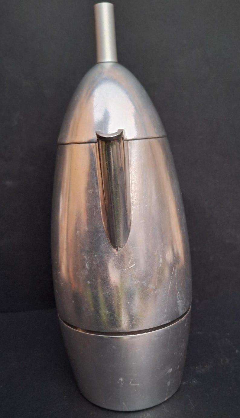 May include: A silver aluminum stovetop espresso maker with a rounded, teardrop shape. The maker has a spout on the side and a removable top.