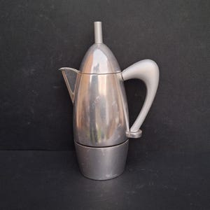 May include: A silver aluminium stovetop espresso maker with a curved handle.